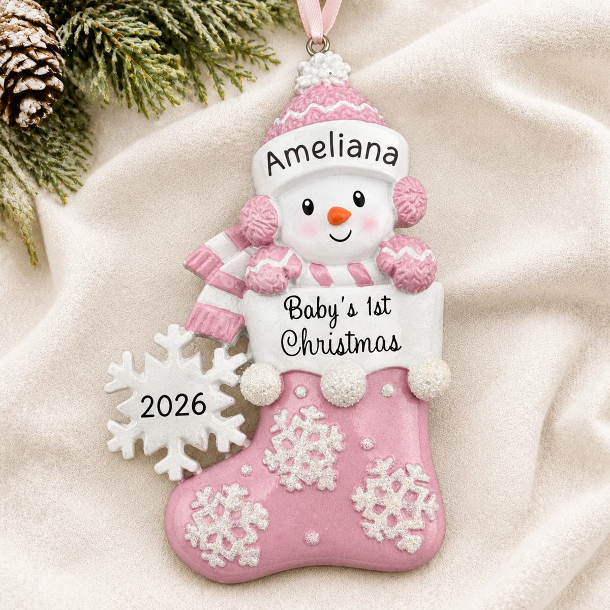 Personalized pink snowman baby's 1st christmas ornament laid on a soft white knit blanket