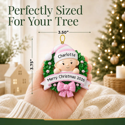 Size guide: the personalized pink baby girl wreath christmas ornament is 3.50 in wide by 3.75 in tall, shown in hand