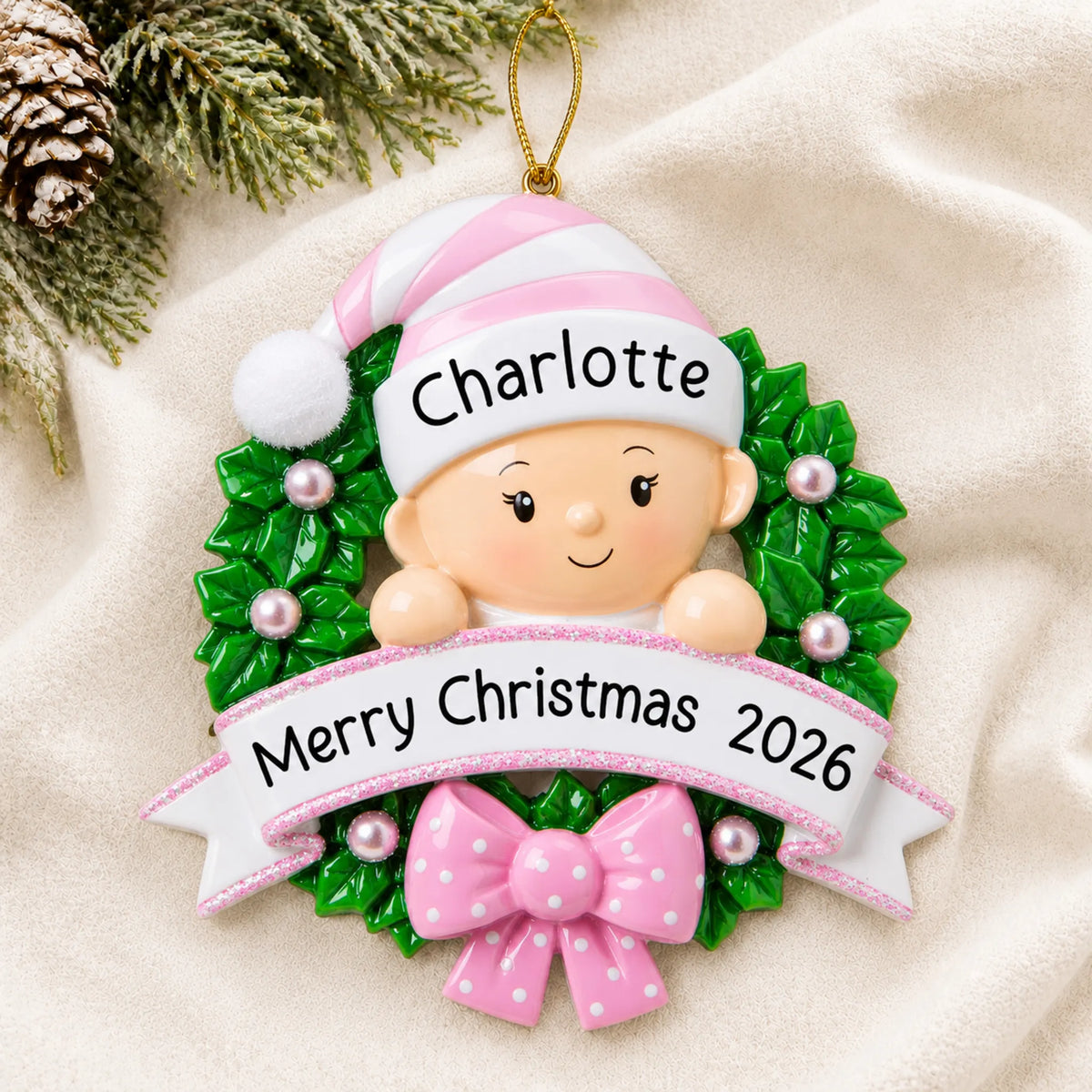 Personalized pink baby girl wreath christmas ornament laid on a soft white knit blanket