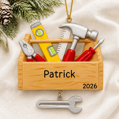 Personalized handyman tool box christmas ornament laid on a soft white knit blanket
