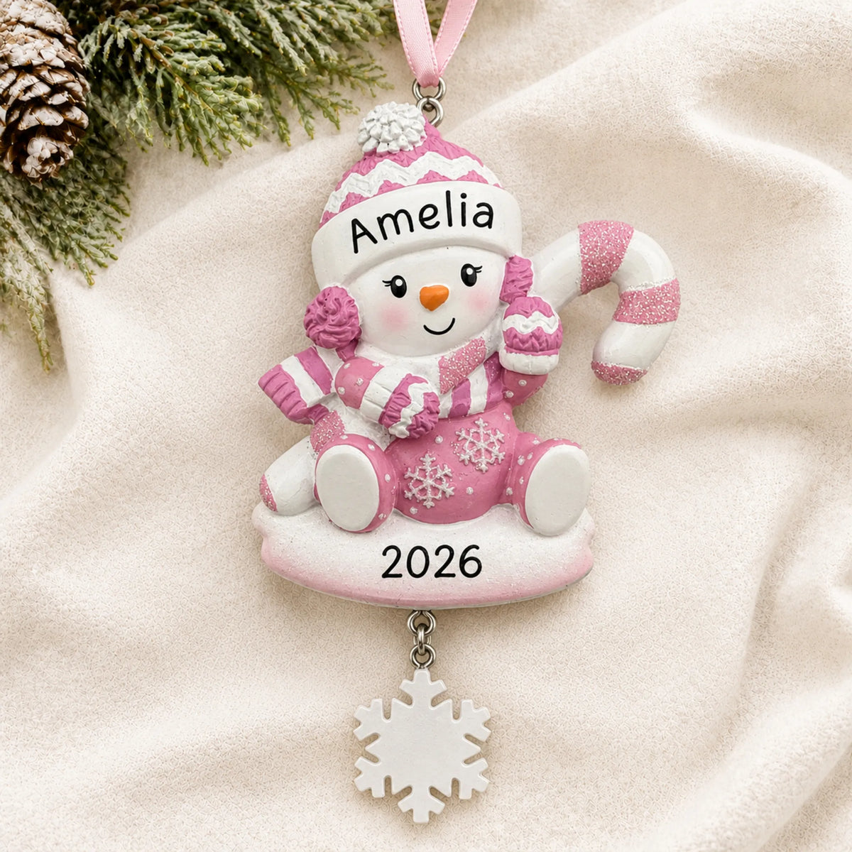 Personalized baby girl snowman christmas ornament laid on a soft white knit blanket
