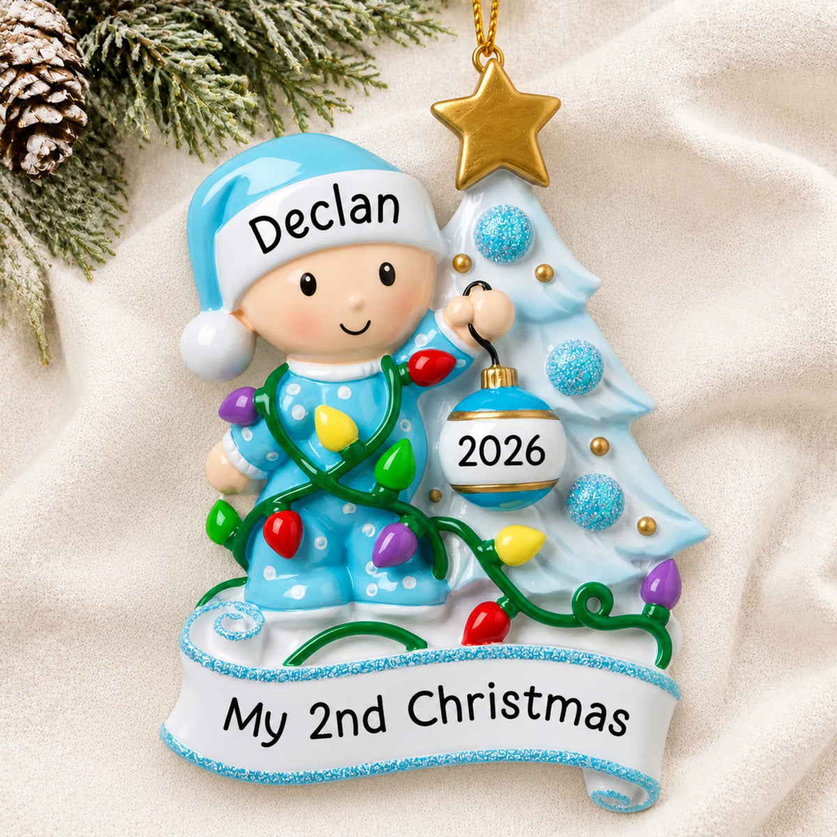 Personalized blue baby's 2nd christmas ornament laid on a soft white knit blanket