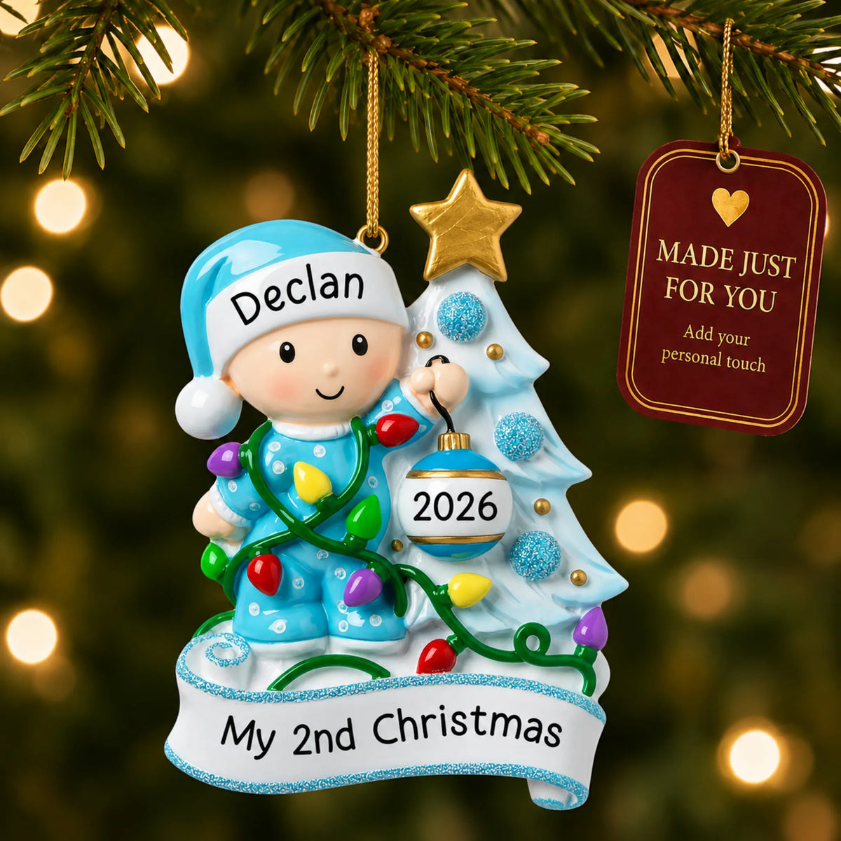 Blue baby's 2nd christmas ornament hanging on a lit Christmas tree with a Made Just For You gift tag