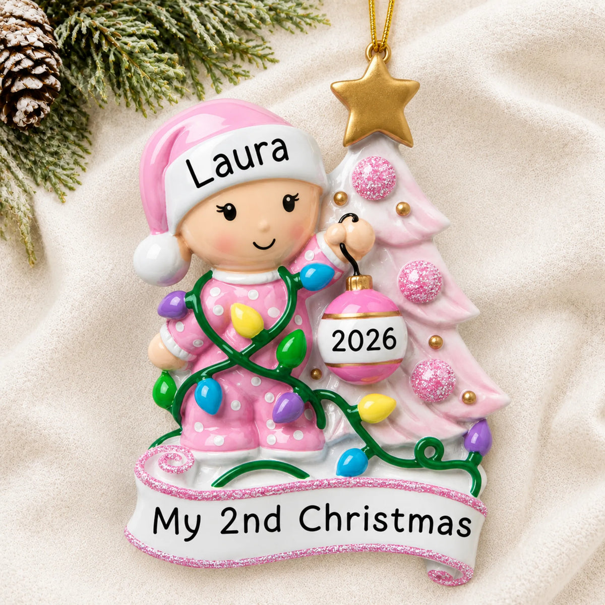Personalized pink baby's 2nd christmas ornament laid on a soft white knit blanket