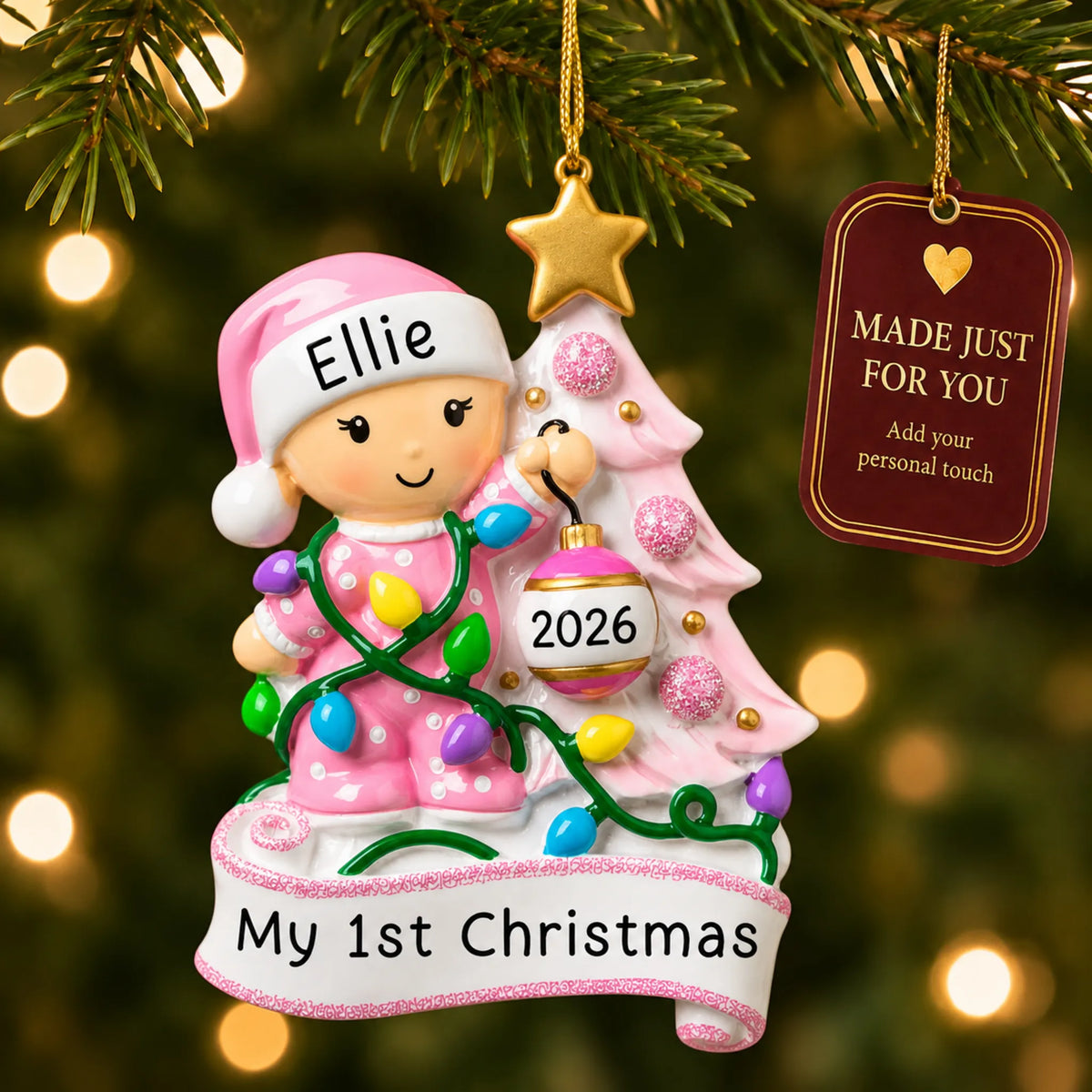 Pink baby's 1st christmas tree ornament hanging on a lit Christmas tree with a Made Just For You gift tag