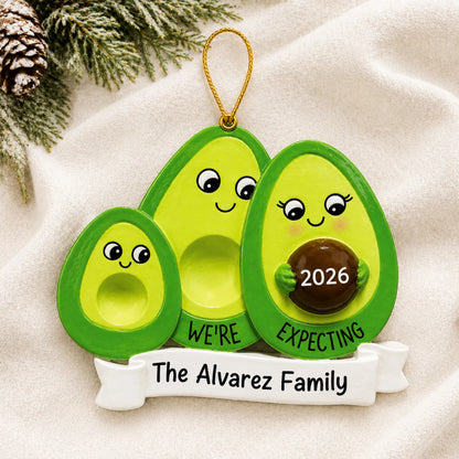 Personalized Avocado Expecting Family of 3 christmas ornament laid on a soft white knit blanket