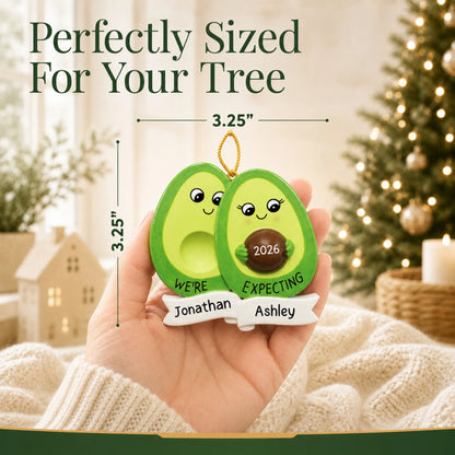 Size guide: the personalized Avocado Expecting Couple christmas ornament is 3.25 in wide by 3.25 in tall, shown in hand