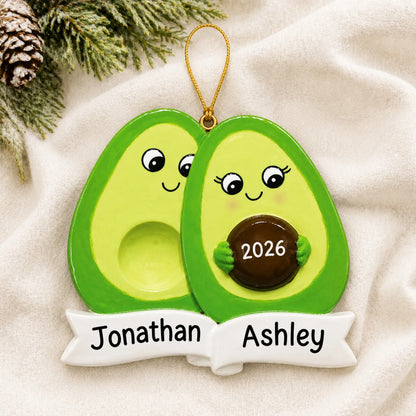 Personalized Avocado Expecting Couple christmas ornament laid on a soft white knit blanket