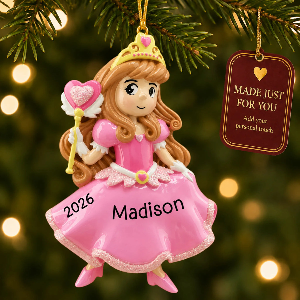 Pink princess christmas ornament hanging on a lit Christmas tree with a Made Just For You gift tag