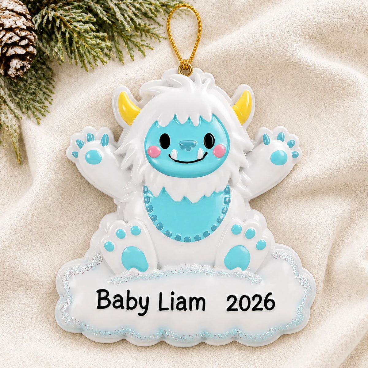 Personalized blue baby boy yeti christmas ornament laid on a soft white knit blanket