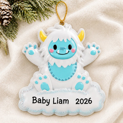 Personalized blue baby boy yeti christmas ornament laid on a soft white knit blanket
