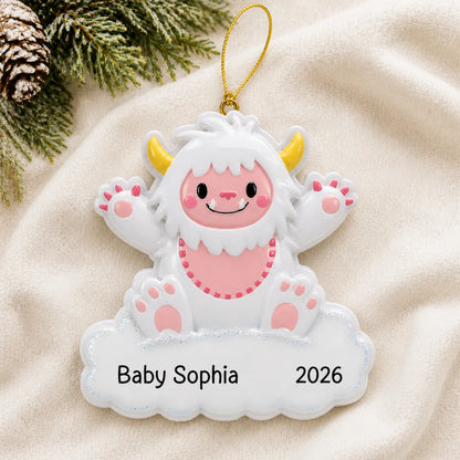 Personalized pink baby girl yeti christmas ornament laid on a soft white knit blanket