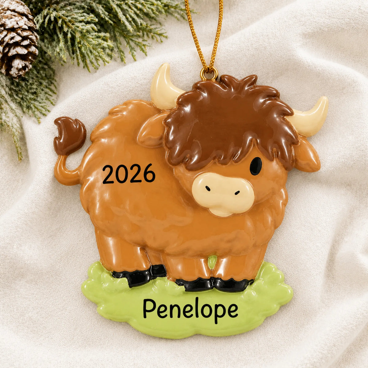 Personalized highland cow christmas ornament laid on a soft white knit blanket