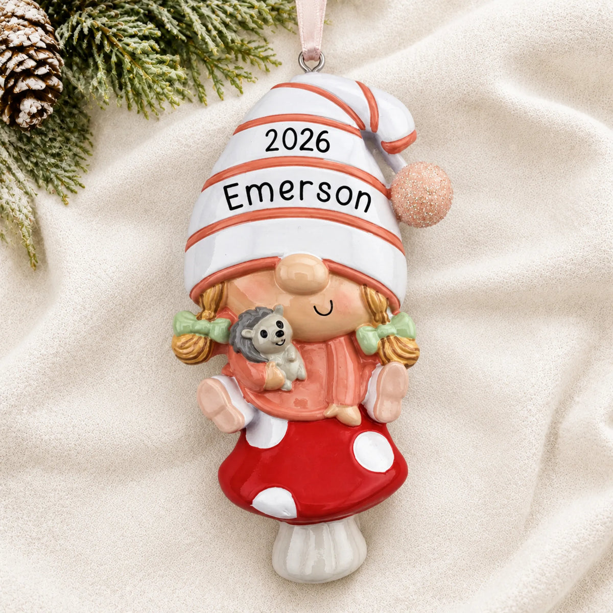 Personalized baby girl gnome christmas ornament laid on a soft white knit blanket