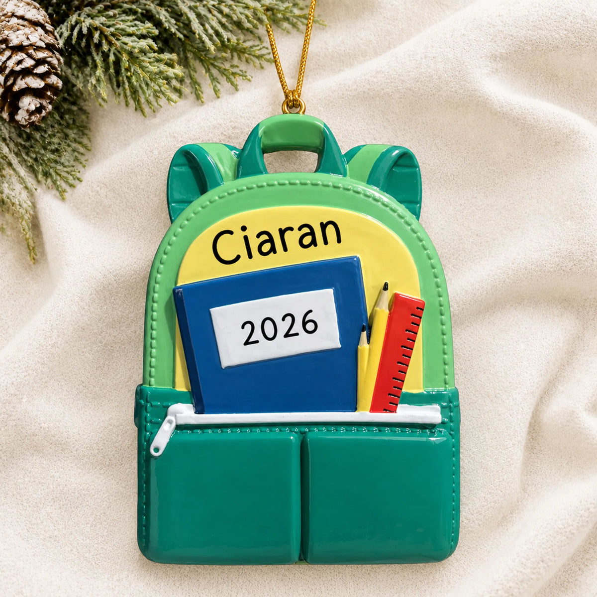 Personalized green school backpack Christmas ornament shown on a soft white blanket