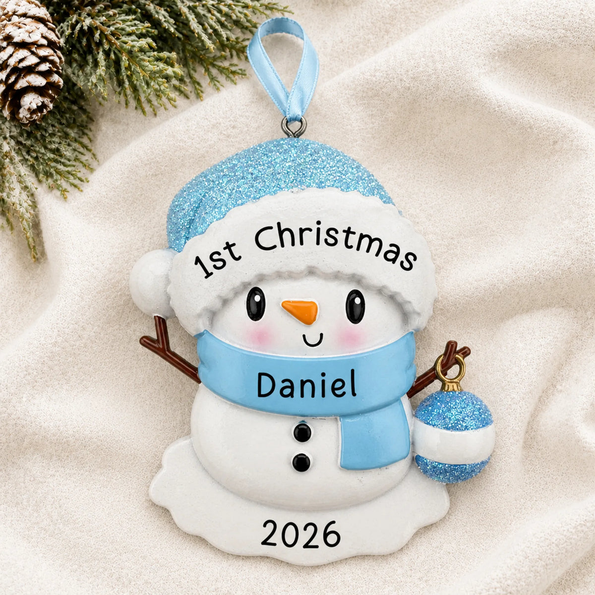 Personalized blue baby snowman christmas ornament laid on a soft white knit blanket