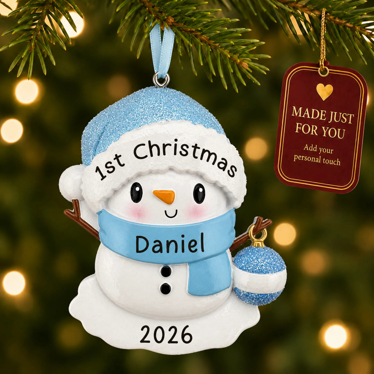 Blue baby snowman christmas ornament hanging on a lit Christmas tree with a Made Just For You gift tag
