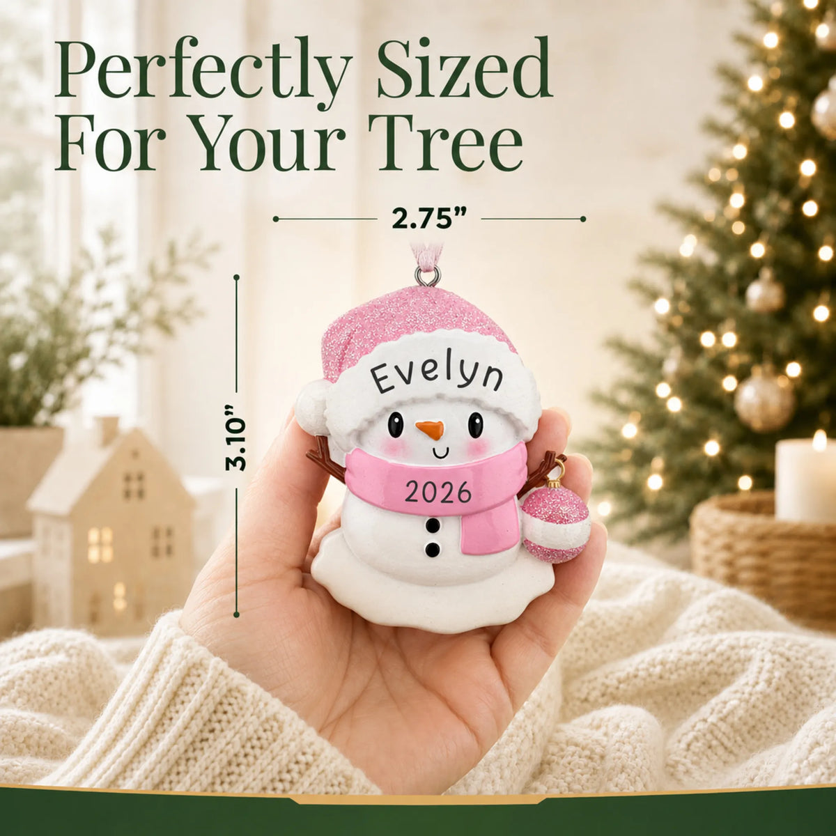 Size guide: the personalized pink baby snowman christmas ornament shown in hand next to a Christmas tree