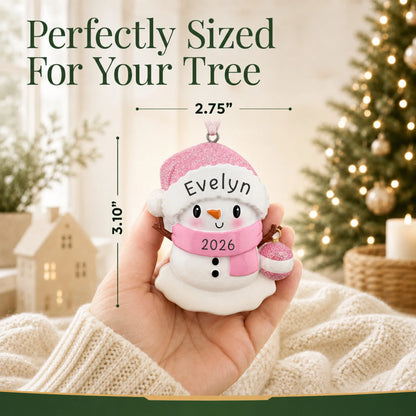 Size guide: the personalized pink baby snowman christmas ornament shown in hand next to a Christmas tree