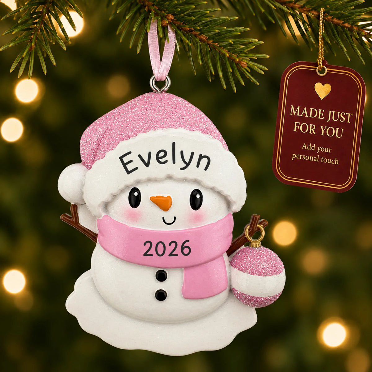 Pink baby snowman christmas ornament hanging on a lit Christmas tree with a Made Just For You gift tag