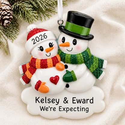 Personalized Expecting Snowman Couple christmas ornament laid on a soft white knit blanket
