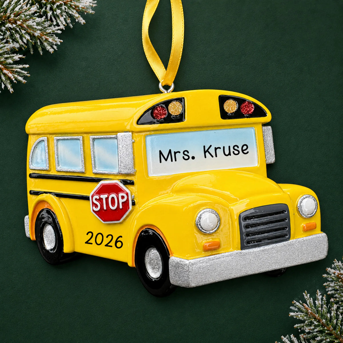 Personalized yellow school bus Christmas ornament with name and year, shown on a green holiday background
