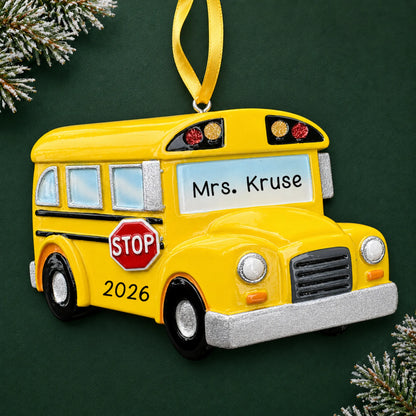 Personalized yellow school bus Christmas ornament with name and year, shown on a green holiday background