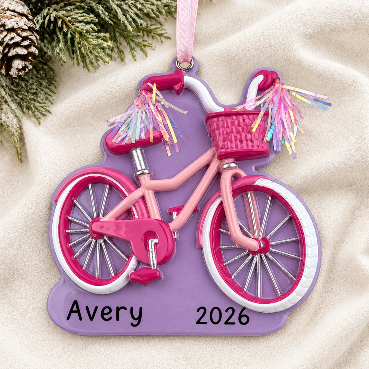 Personalized girl's first bike christmas ornament laid on a soft white knit blanket
