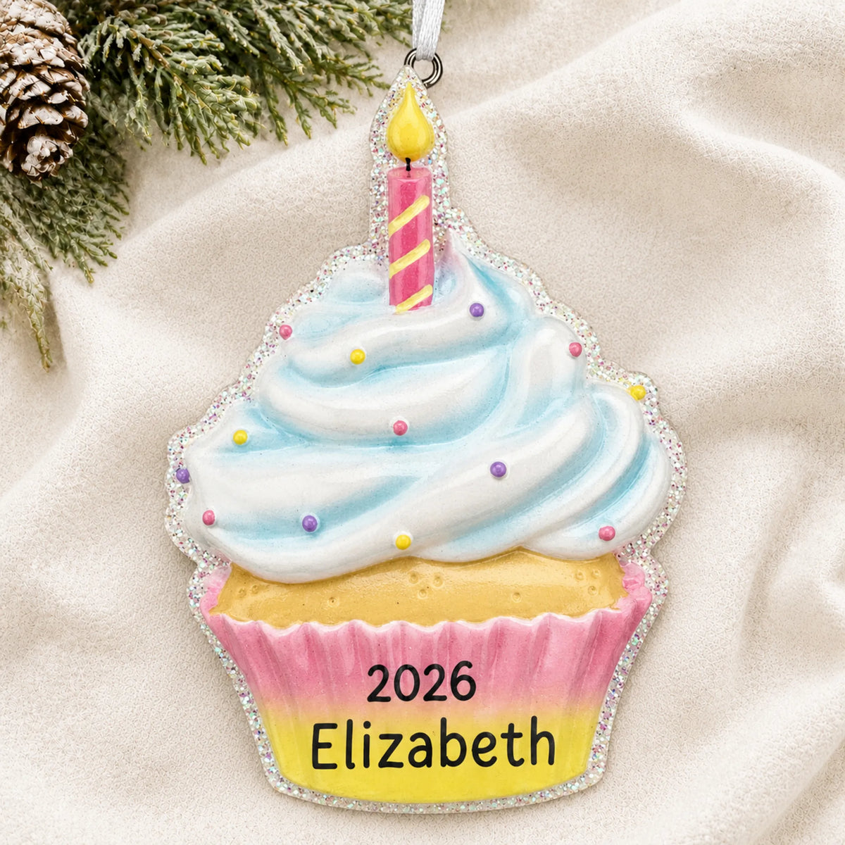 Personalized birthday cupcake christmas ornament laid on a soft white knit blanket