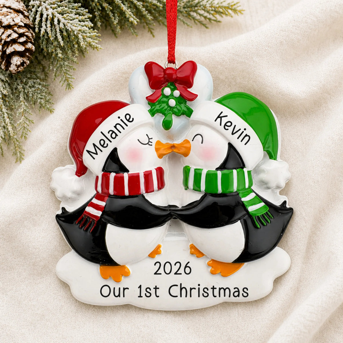 Personalized penguin mistletoe kisses couple christmas ornament laid on a soft white knit blanket