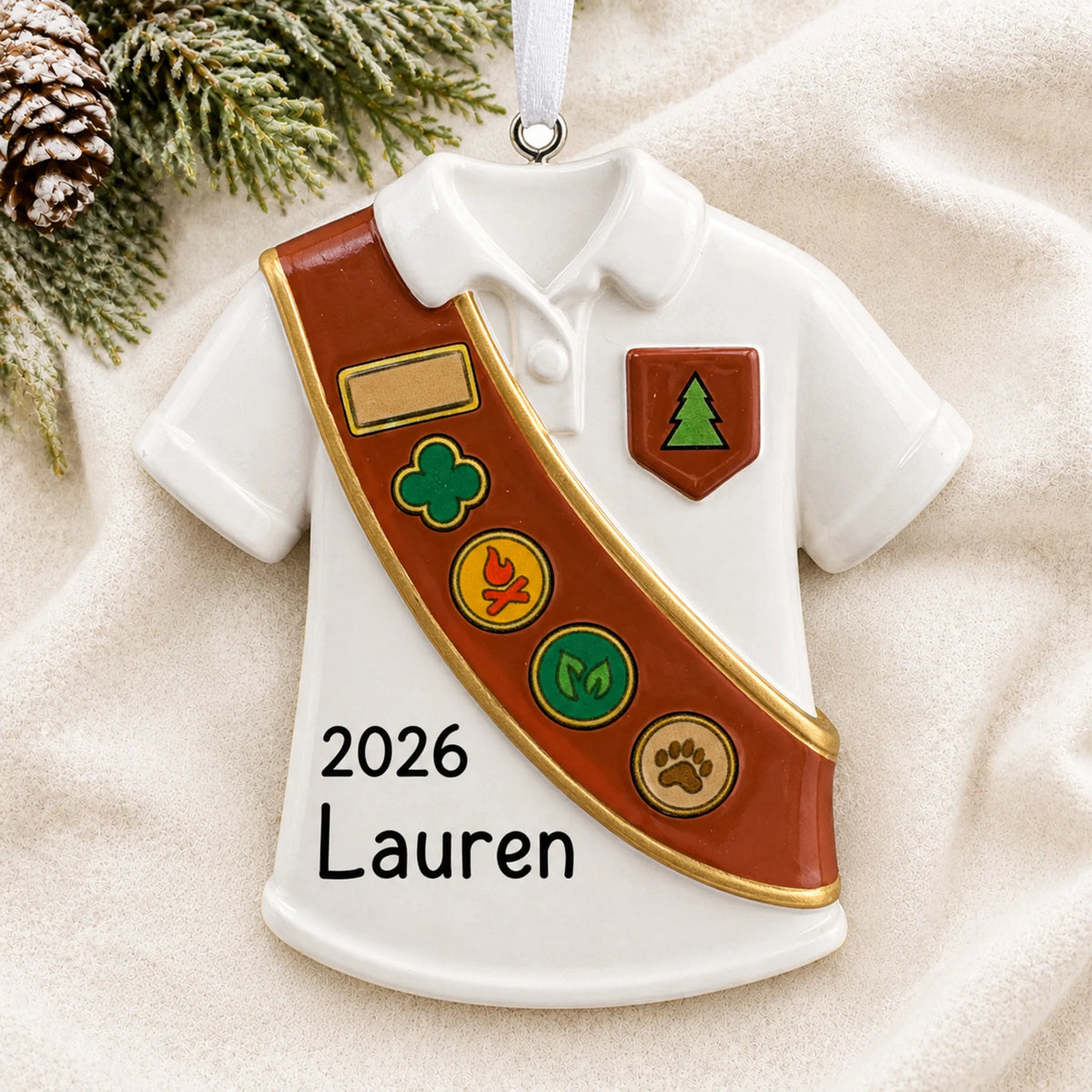 Personalized Girl Scout brown sash christmas ornament laid on a soft white knit blanket