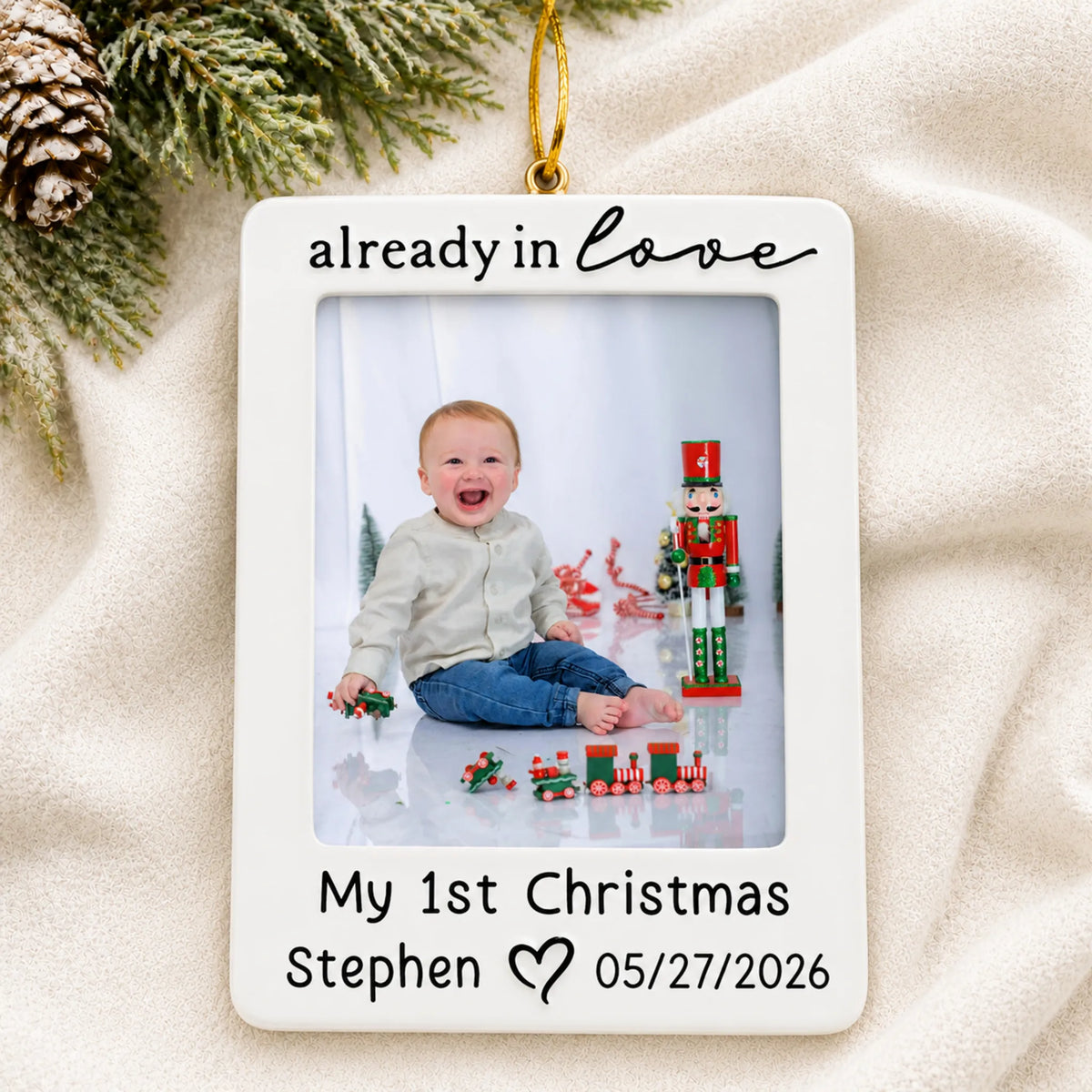 Personalized already in love baby photo frame christmas ornament laid on a soft white knit blanket