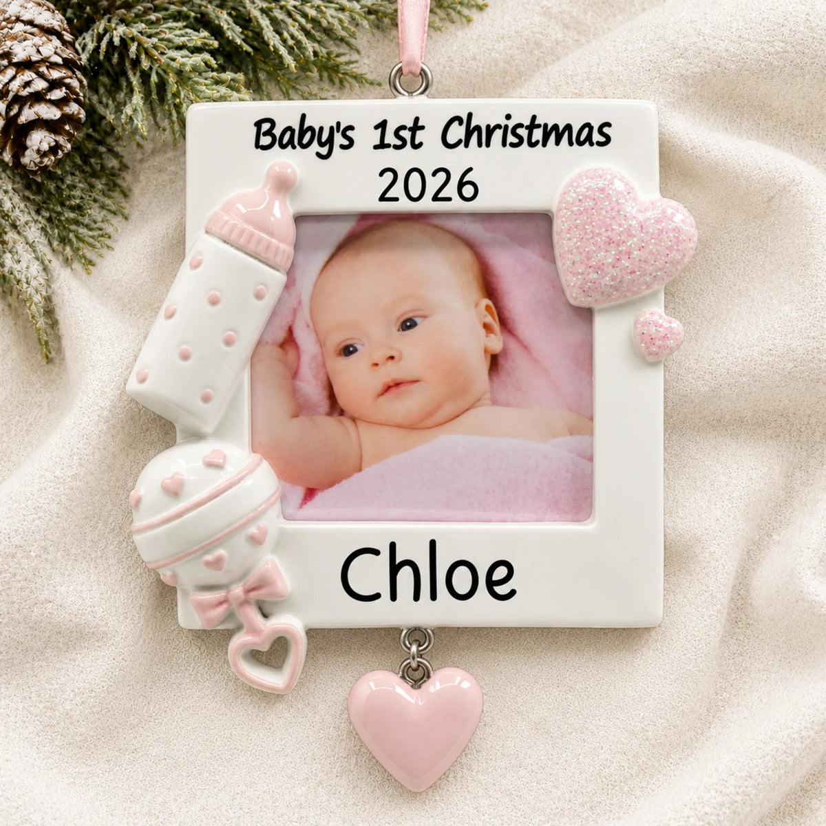 Personalized pink baby's first picture frame christmas ornament laid on a soft white knit blanket