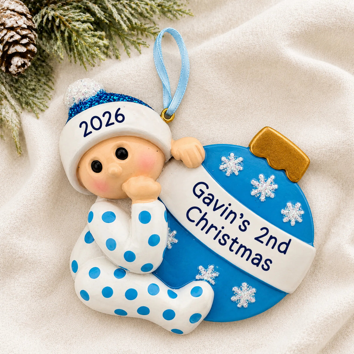Personalized blue baby's 2nd christmas ornament laid on a soft white knit blanket