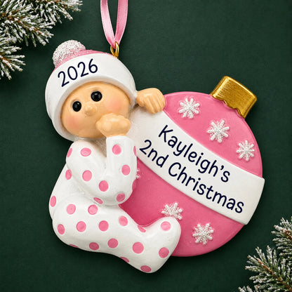 Personalized pink baby's 2nd christmas ornament on a dark green pine background