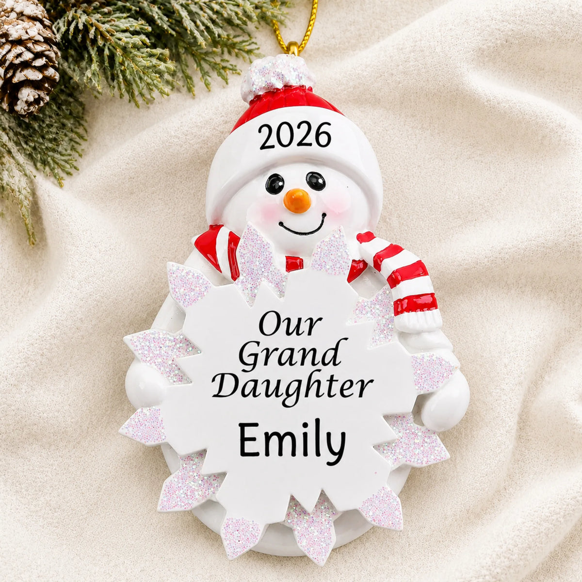 Personalized granddaughter snowman christmas ornament laid on a soft white knit blanket