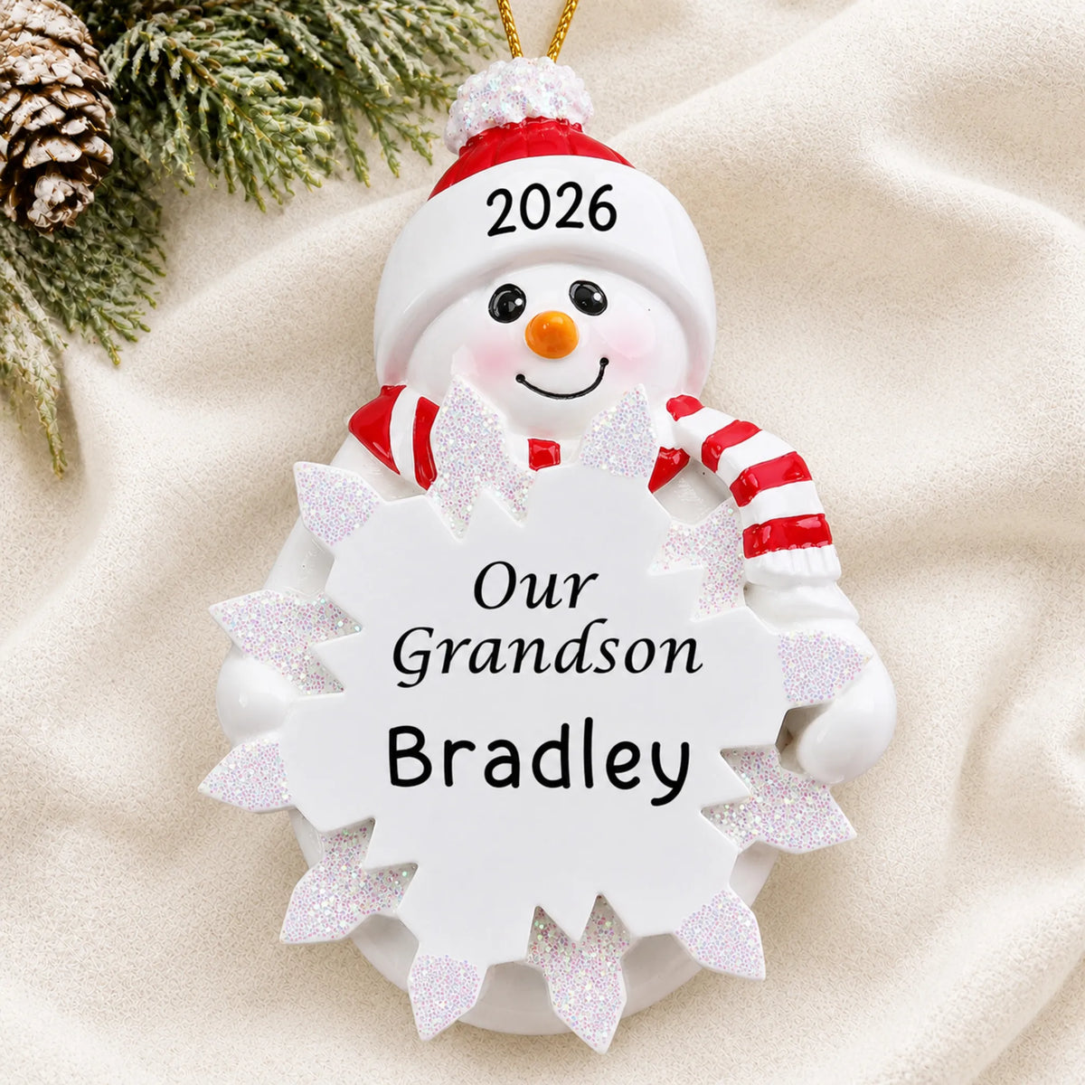 Personalized grandson snowman christmas ornament laid on a soft white knit blanket
