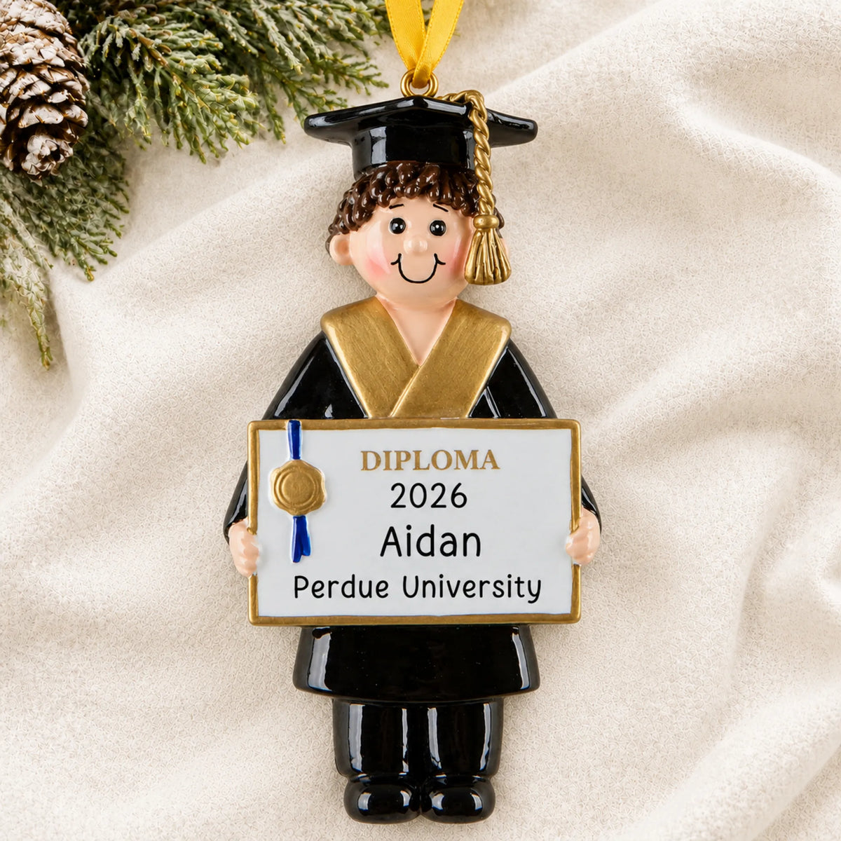 Personalized graduation boy Christmas ornament with diploma, name and year, shown on a soft white blanket