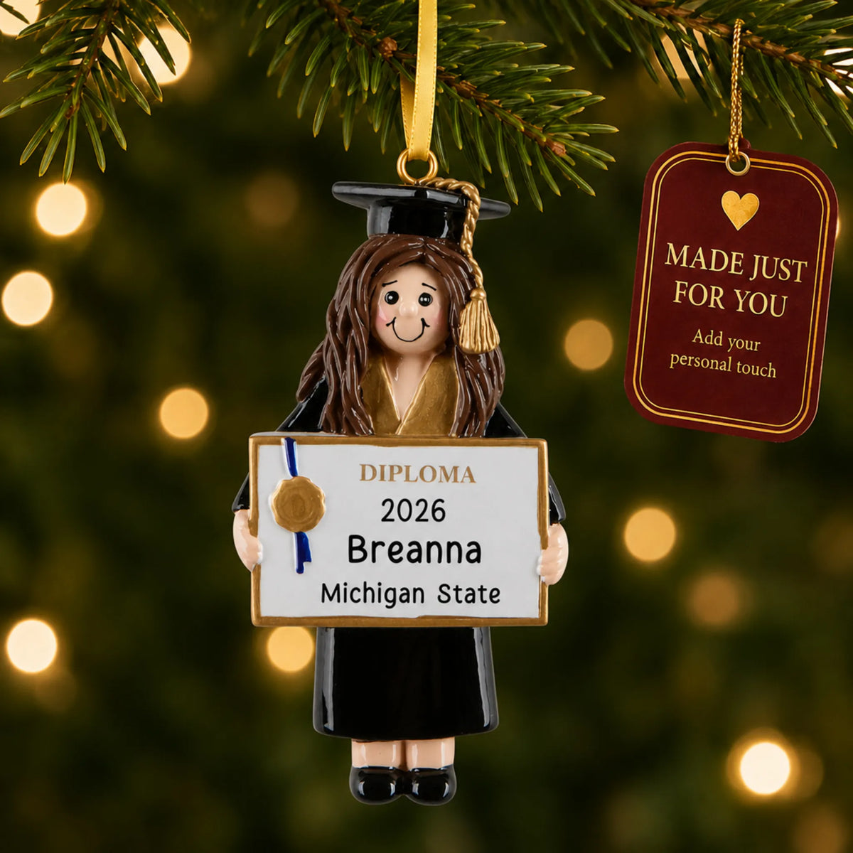 Personalized graduation girl Christmas ornament hanging by a gold ribbon among tree lights with a Made Just For You tag