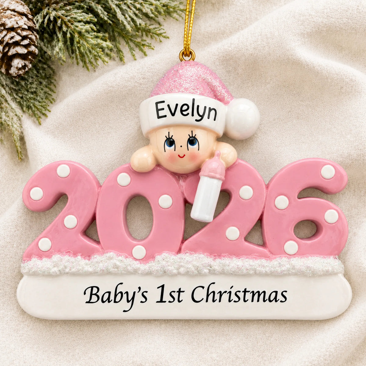 Personalized baby girl's 1st christmas 2026 ornament laid on a soft white knit blanket