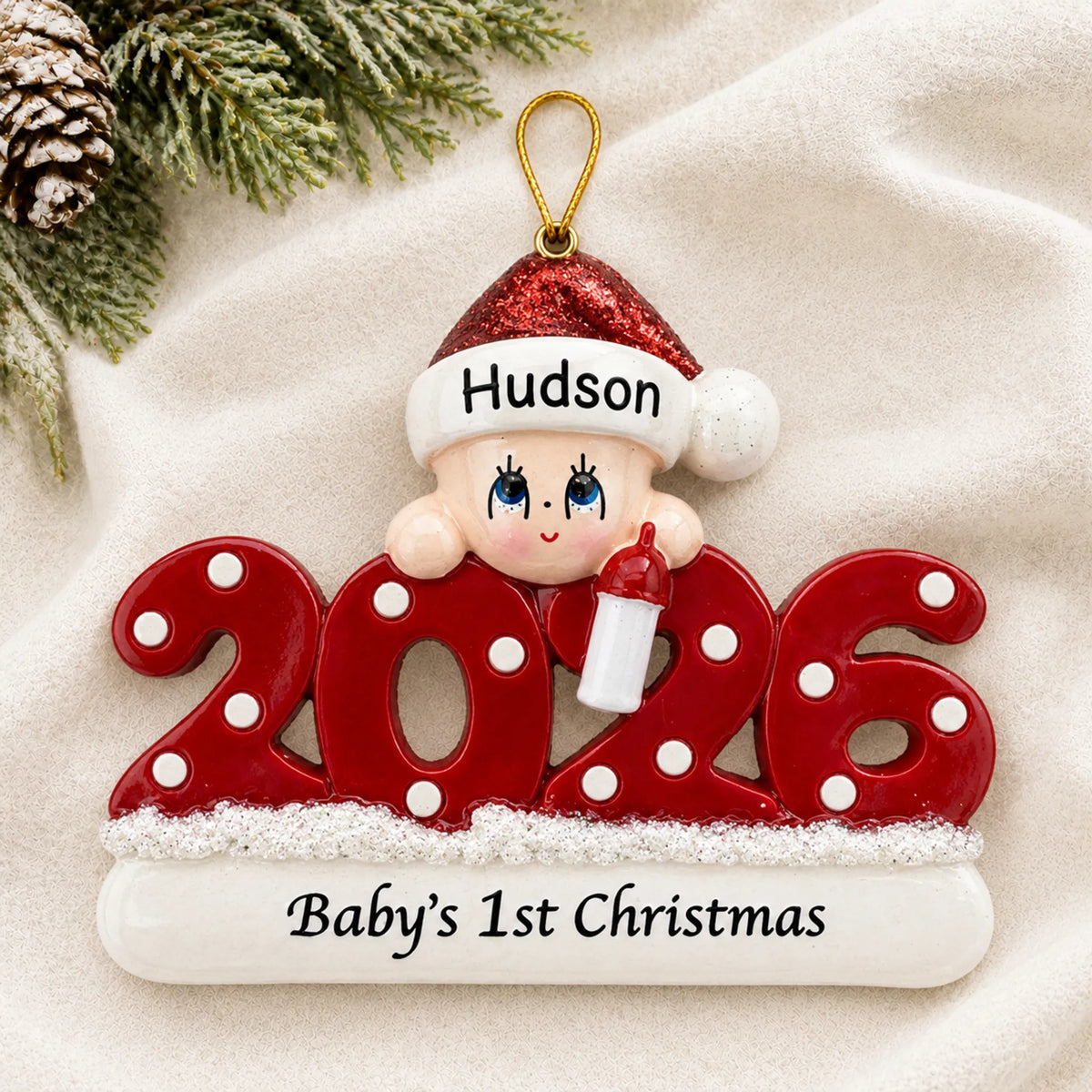 Personalized baby's 1st christmas 2026 ornament laid on a soft white knit blanket