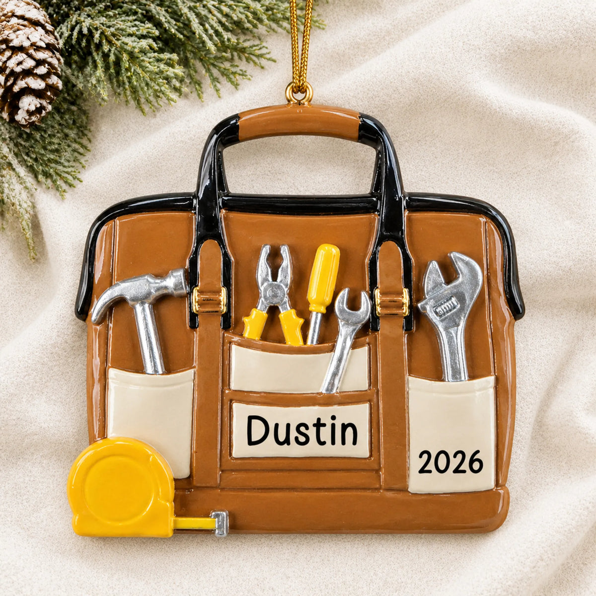 Personalized tool bag handyman christmas ornament laid on a soft white knit blanket