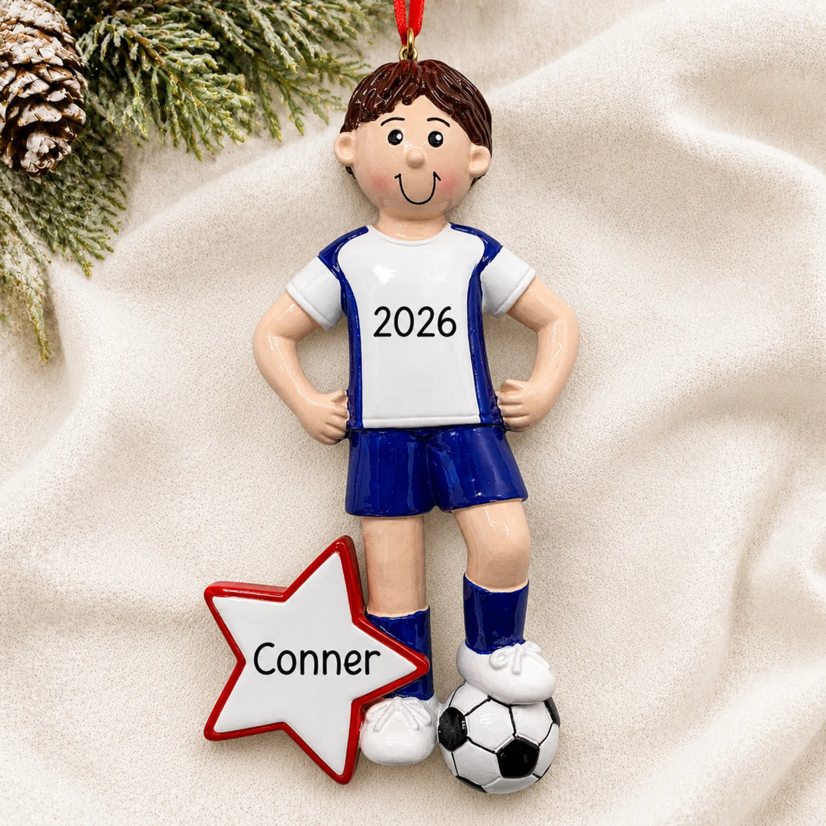 Personalized soccer all-star boy christmas ornament laid on a soft white knit blanket