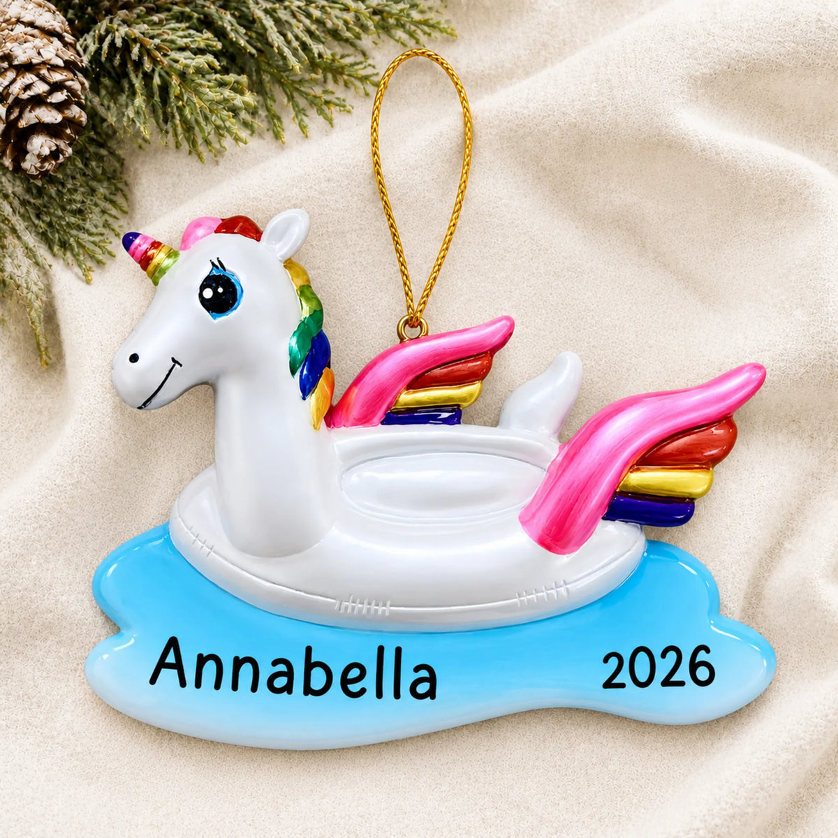 Personalized unicorn floatie christmas ornament laid on a soft white knit blanket