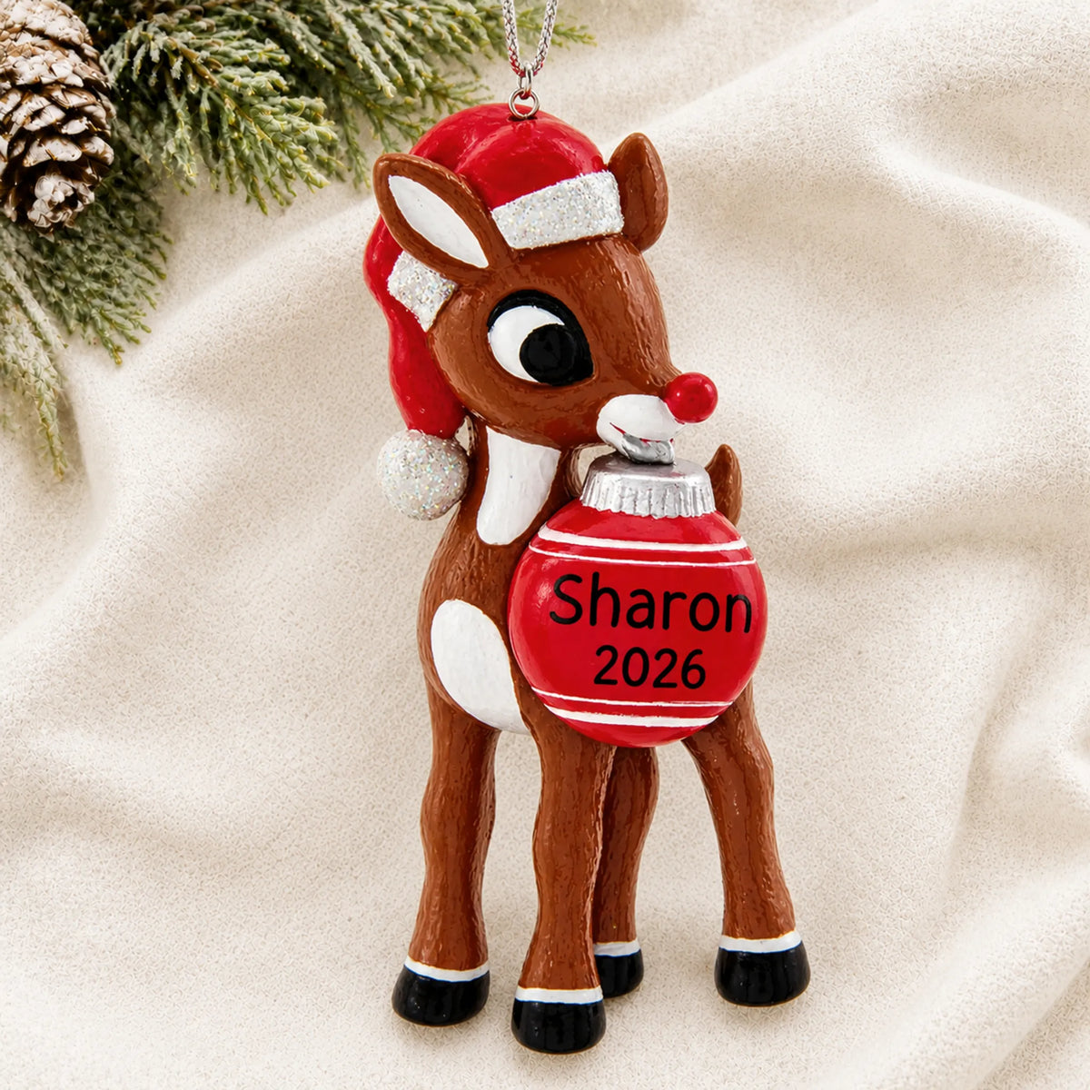 Personalized Rudolph the Red-Nosed Reindeer christmas ornament laid on a soft white knit blanket