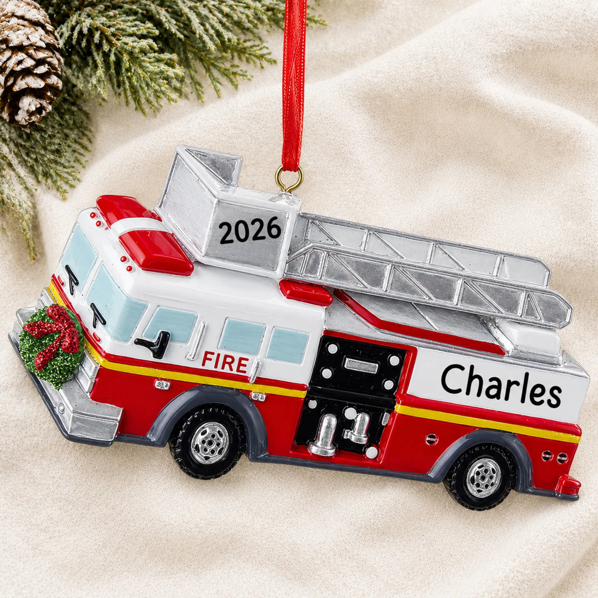 Personalized fire truck with ladder christmas ornament laid on a soft white knit blanket