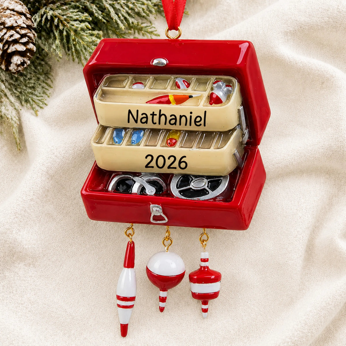 Personalized fishing tackle box christmas ornament laid on a soft white knit blanket